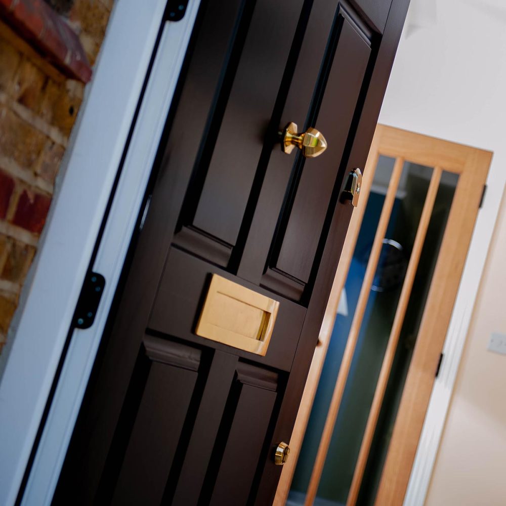 A black timber entrance door with polished brass ironmongery