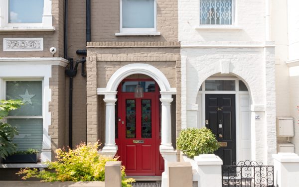 A timber front door painted red with stained glass. There are columns either side, with neighbouring properties.